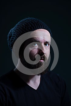 authentic dramatic portrait of a millennial with a beard in a black knitted hat, on a dark background