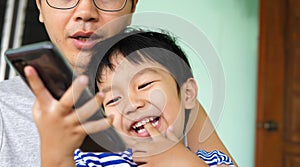 Authentic father and son looking on smartphone outdoor with happy smiling face. Dad and child have happy moment together.