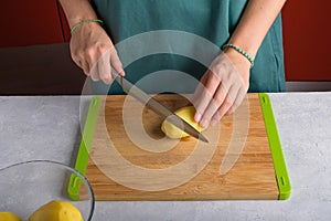 Authentic female hands cutting potatoes on wooden cutting board on gray kitchen table