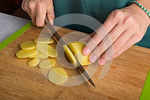 Authentic female hands cutting potatoes on wooden cutting board on gray kitchen table