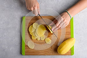 Authentic female hands cutting potatoes on wooden cutting board on gray kitchen table