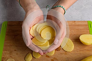 Authentic female hands holding cutting potatoes on wooden cutting board on kitchen table background