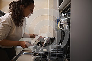 Authentic housewife taking out kitchen clean and sterilize kitchen utensils from an overload automatic dishwasher