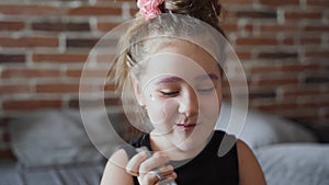 Authentic little girl chews and laughs. She is holding a fork. She smiles and laught. A brick wall is visible in the background