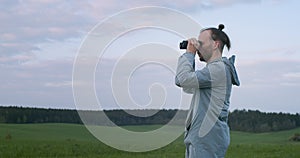 Authentic man looking into field glass on green field background copy space. Side view of traveler tourist observing
