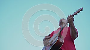 authentic man plays acoustic string guitar against clear blue sky