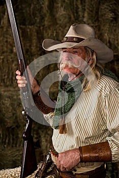 Authentic old west cowboy with shotgun, hat and bandanna in stable portrait photo