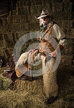 Authentic old west cowboy with shotgun, hat and bandanna in stable portrait