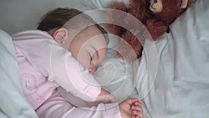 Authentic portrait cute caucasian little infant chubby baby girl or boy in pink sleep with teddy bear on white bed