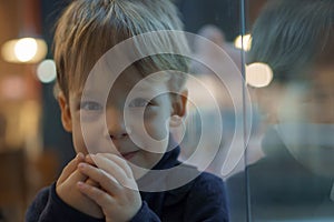 authentic portrait little handsome blond smiling boy sitting in cafe in evening alone. Preschool toddler kid child