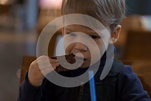 authentic portrait little handsome blond smiling boy sitting in cafe in evening alone. Preschool toddler kid child