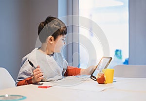 Authentic Portrait of preschool kid using tablet for his homework, New normal life child boy use touch pad for home learning, E- photo
