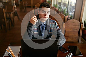 Authentic portrait of young confident businessman looking at camera with laptop tablet and smartphone on table. Hipster