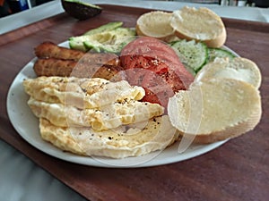 Authentic power breakfast with x sausage avocado tomatoes cucumber and toasted baguettes on a brown surface