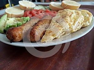 Authentic power breakfast with x sausage avocado tomatoes cucumber and toasted baguettes on a brown surface