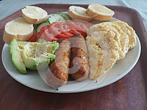 Authentic power breakfast with x sausage avocado tomatoes cucumber and toasted baguettes on a brown surface