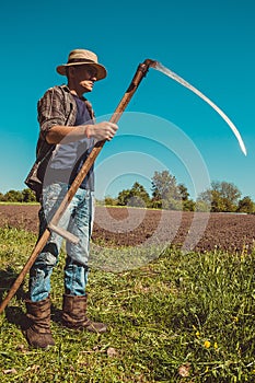 Authentic rural farmer with scythe. Agriculture worker. Sharp blade. Vegetable garden. Farm implements. Rustic background. Work