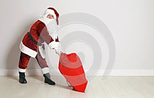Authentic Santa Claus with bag full of gifts against grey wall