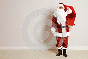 Authentic Santa Claus with bag full of gifts against grey wall