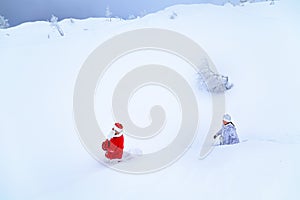 Authentic Santa Claus and a girl in winter clothes are walking on a snowy mountain