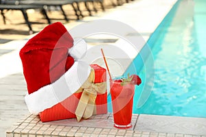 Authentic Santa Claus hat, gift box and cocktail near pool