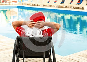 Authentic Santa Claus resting on lounge chair near pool at resort