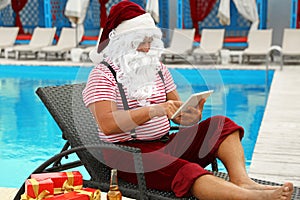 Authentic Santa Claus with tablet resting on lounge chair