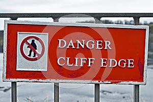 Authentic sign for danger cliff edge with crossed out icon of person walking. Blurred sea background.