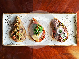 Authentic traditional spanish tapas set on wooden table for lunch, top view. Selection of bruschetta on crusty bread.