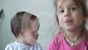 authentic two joyful happy children, infant baby and 3-4 year old girl siting together on blue and white bed close up