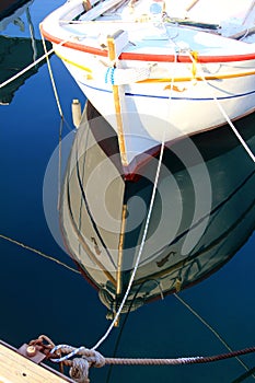 Authentic white wooden boat and ropes on crystal clear sea waters and the sun reflection, calm water and cordage in the soft