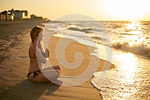 Authentic woman in swimsuit doing yoga padmasana on the beach in the morning. Real unretouched shape girl silhouette in