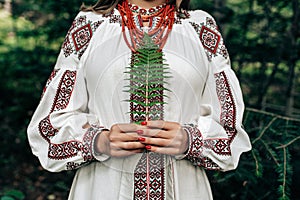 Authentic woman in traditional ukrainian costume with fern in forest.