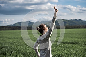 Authentic young woman standing under dramatic spring sky with her arm raised in victorious gesture