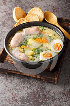 Authentic zurek a hearty Polish sour rye soup with rich white sausage and fresh veggies close-up in a bowl. Vertical