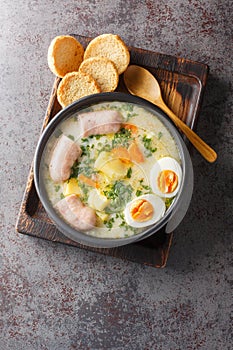 Authentic zurek a hearty Polish sour rye soup with rich white sausage and fresh veggies close-up in a bowl. Vertical top view