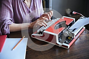 Authoress sitting at the table and typing on typerwriter indoors