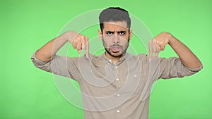 Authoritative brunette man pointing down with angry bossy expression and saying here. green background, chroma key