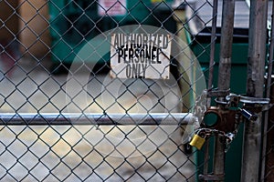 Authorized personnel sign on a chain link fence with dumpsters