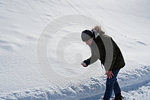 Autisitic teenager boy picking snow in order to feel it and observe it