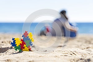 Autism awareness day concept. Puzzle heart on the sand and silhouette of mother hugging the child on the beach and