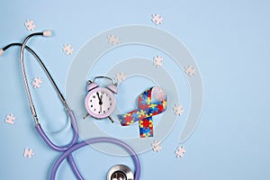 Autism concept with puzzle awareness ribbon, stethoscope and alarm clock on a blue background