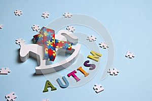 Autism concept with toy rocking horse and and puzzle awareness ribbon on a blue background