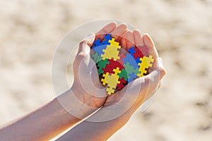 Autism friendly holidays. Child hands holding colorful heart in the beach over sand