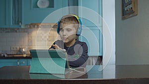 Autistic boy using tablet computer with headphones on the kitchen. Kid with autism looking around at home. Autism