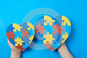 Autistic kid hands holding jigsaw puzzle heart shape. Autism spectrum disorder family support concept. World Autism