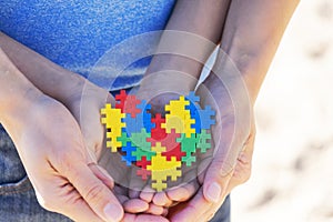 Autistic kid hands supported by mother holding multicolored puzzle heart. World autism awareness day concept