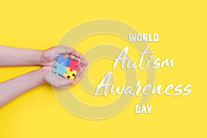 Autistic pride day. The hands of a small child holding colorful puzzles on yellow background. Heart of puzzles. Banner
