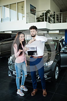 Auto business, car sale, consumerism and people concept - happy woman with car dealer look at pappers in auto show or salon