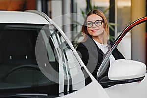 Auto business, car sale, consumerism and people concept - happy woman taking car key from dealer in auto show or salon
